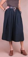 Woman wearing a high-waisted black midi skirt with belt and brown mules