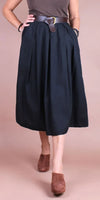 Woman wearing a black pleated midi skirt with brown belt and brown suede mules
