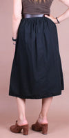 Back view of woman wearing a black midi skirt with a fitted waistband and brown heeled mules