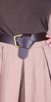 Close-up of brown leather belt with gold buckle over pleated beige skirt and taupe top