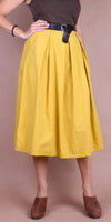 Woman wearing a yellow pleated midi skirt with a black belt and brown shoes