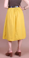 Woman wearing a yellow midi skirt with pleats, brown sleeveless top, and brown heeled mules
