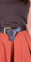 Woman wearing a brown ribbed top, wide black leather belt with brass buckle, and rust skirt