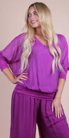 Woman wearing a purple silk blouse and wide-leg pants, relaxed fit, neutral background