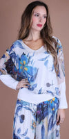 Woman wearing white floral silk blouse and matching wide-leg pants with blue and yellow print