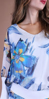 Woman wearing a white blouse with blue and yellow floral print and wide neckline