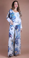 Woman wearing a flowy floral print blouse and wide-leg pants set against tan background