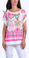 Woman wearing a colorful patterned silk blouse with short sleeves and white pants