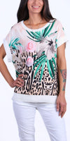 Woman wearing tropical floral and animal print top with short sleeves and white pants