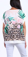 Woman wearing short-sleeve top with leopard print, floral and palm leaf design, and white pants