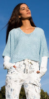 Woman wearing light blue crochet top and floral print pants, outdoors in sunlight