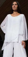 Woman wearing a white flowy silk blouse and wide-leg pants, standing outdoors