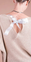 Close-up of a woman wearing a beige knit top with a back keyhole and satin bow detail