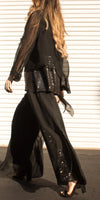 Woman wearing black sheer blouse with sequin details and wide-leg pants outdoors