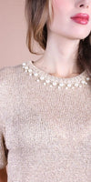Woman wearing a beige metallic knit top with pearl embellished neckline