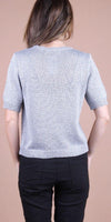 Back view of woman wearing a short-sleeve silver knit top and black pants