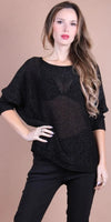 Woman wearing a sheer black knit top and black pants against a beige background