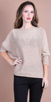 Woman wearing a loose-knit beige sweater with black pants, neutral background.