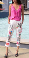 Woman in pink lace camisole and white embroidered linen pants by a pool