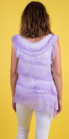 Back view of woman in layered lavender sleeveless top and white pants on yellow background