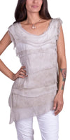 Woman wearing a layered beige tunic top with cap sleeves and white pants