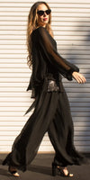 Woman in flowing black silk outfit, wide-leg pants, sheer sleeves, and sunglasses outdoors