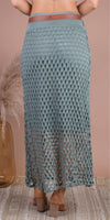 Back view of a woman wearing a blue crochet mesh maxi skirt with heeled sandals and a brown belt.