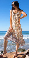 Woman wearing a flowy patterned sundress on a rocky beach with ocean in the background