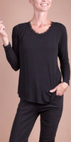Woman wearing a black long sleeve top with lace trim and black pants, neutral background