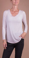 Woman wearing light pink long sleeve top with lace trim neckline and black pants