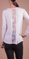 Back view of a woman wearing a light pink long sleeve top with lace panel detail and black pants