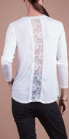 Woman wearing white long sleeve top with sheer lace back panel, black pants