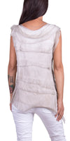 Back view of woman wearing sleeveless layered beige silk top and white pants