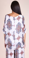 Woman wearing a sheer, patterned white blouse and pants with ornate geometric designs