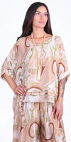 Woman wearing a loose beige and green swirl print silk blouse and pants set with long necklace