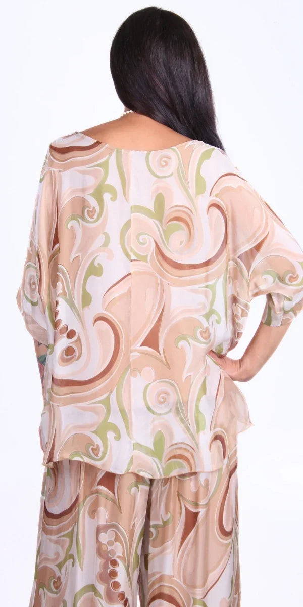 Woman wearing beige and green abstract print silk top and matching pants, back view