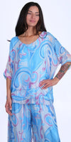 Woman wearing a light blue and lavender swirl print silk blouse and matching pants