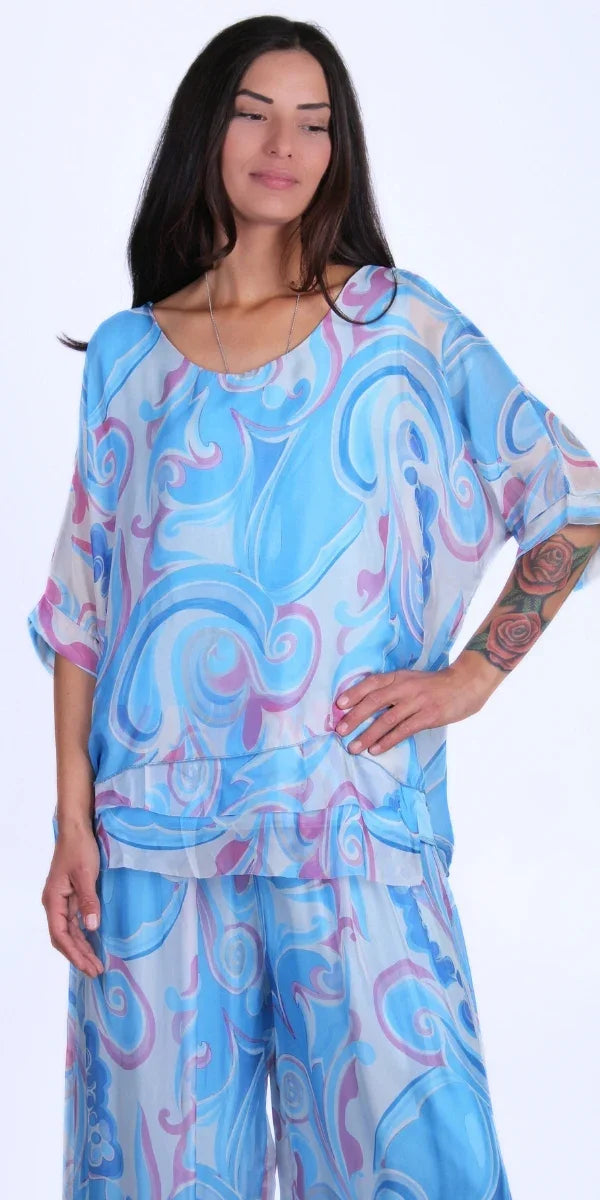 Woman wearing a light blue and lavender swirl print silk blouse and matching pants