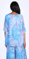 Woman wearing flowy blue and purple swirl print silk top and pants set, back view