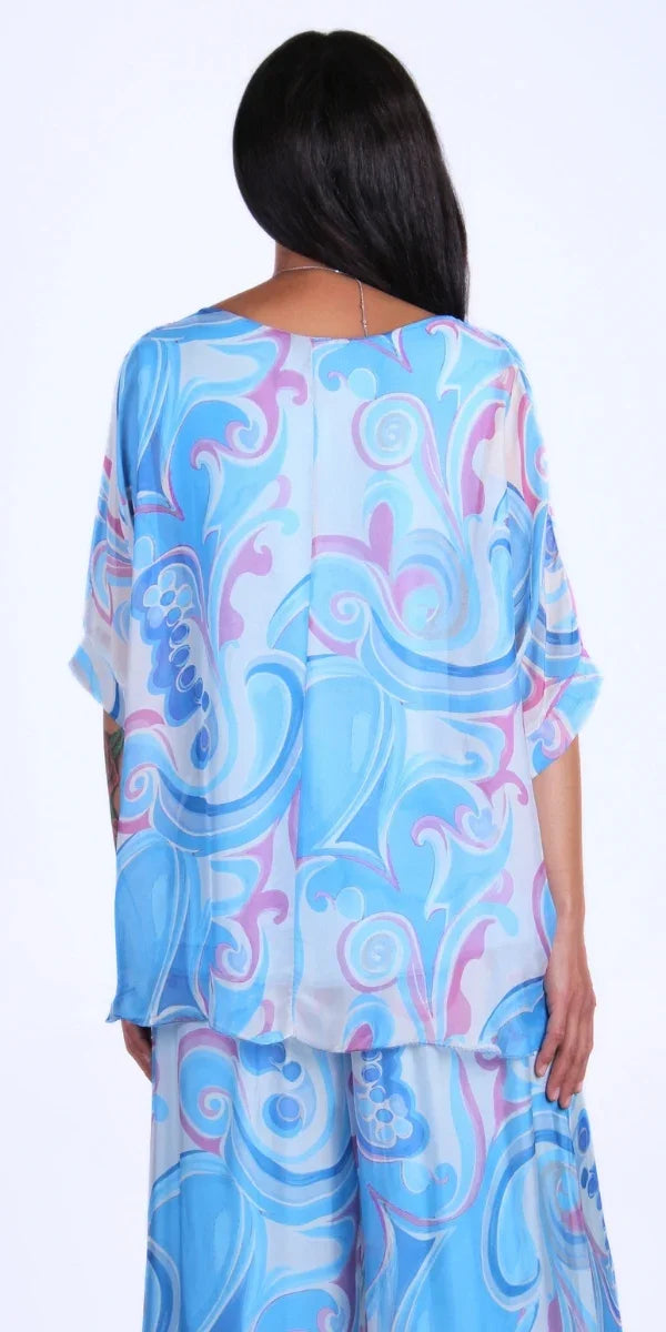 Woman wearing flowy blue and purple swirl print silk top and pants set, back view