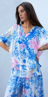 Woman wearing lightweight floral print blouse and skirt in blue and pink tones