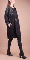Woman wearing black long-sleeve dress with sequin shoulder detail, black leggings, and ankle boots