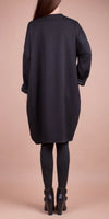 Back view of a woman wearing a loose black long-sleeve tunic dress with leggings and heeled boots