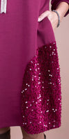 Detail of a fuchsia dress with a hand in the pocket, featuring sequined fabric accent