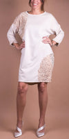 Woman wearing a cream long sleeve dress with sequin patch details, standing against a beige background.