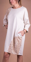 Woman wearing a cream long sleeve dress with gold sequin accents and pockets