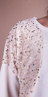 Close-up of cream sequin embellished sleeve on women's top, textured fabric detail