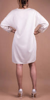 Back view of woman wearing a loose long-sleeve cream sweater dress and white heels
