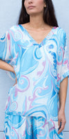 Woman wearing a loose-fitting blue and white patterned silk blouse and pants set
