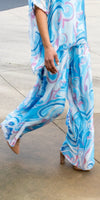 Woman wearing flowy blue and pink swirl print pants and matching top outdoors